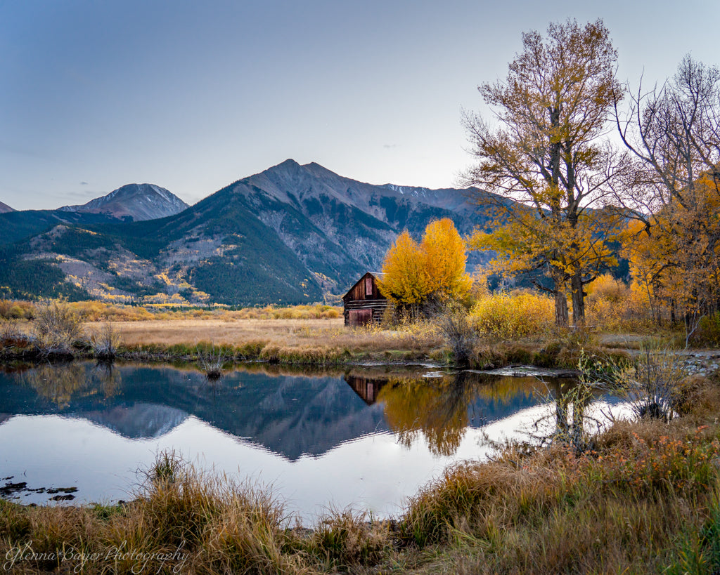 old log Cabin behind pond in front of colorado mountains