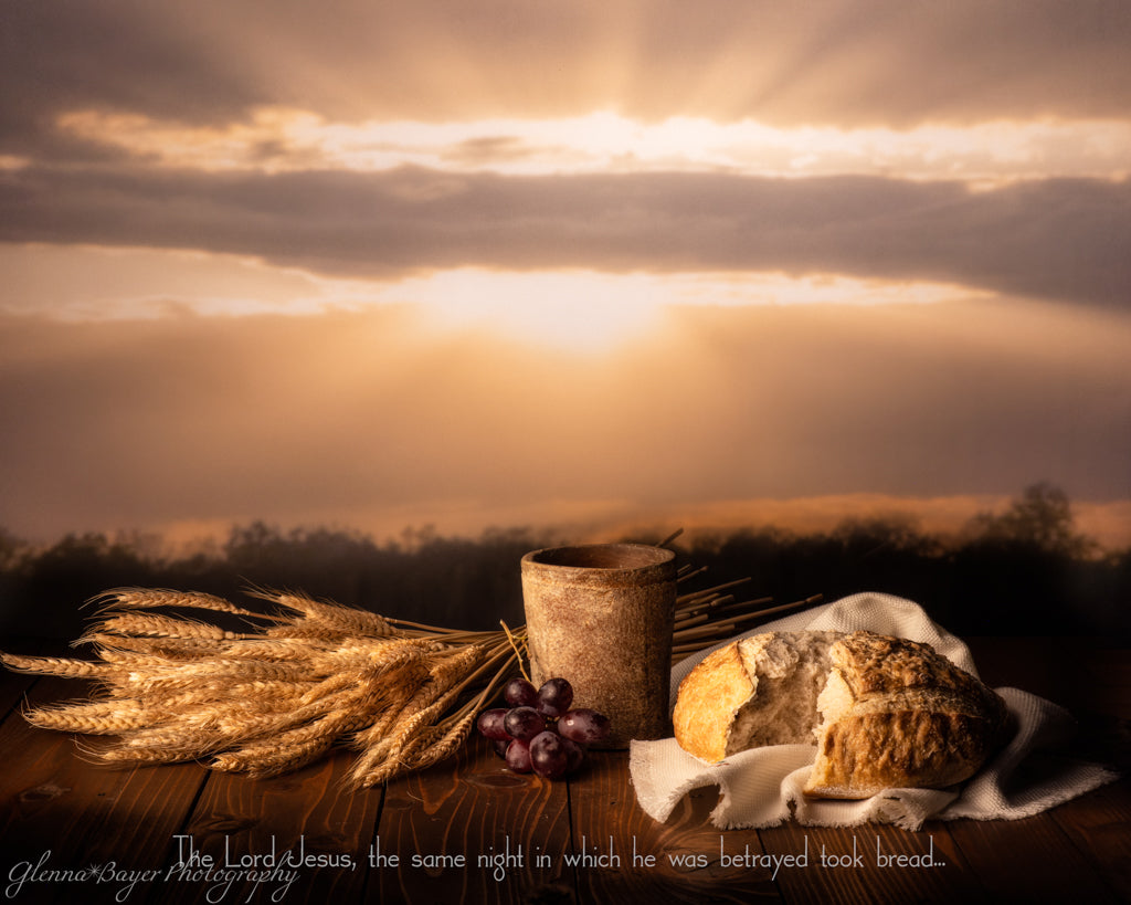still life with bread, grapes, wheat, and a cup with sunset as backdrop