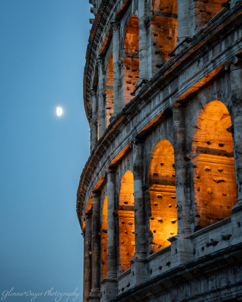 Colosseum lit up at night with moon in background