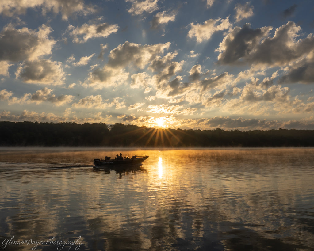 fisherman in boat on foggy lake at sunrise