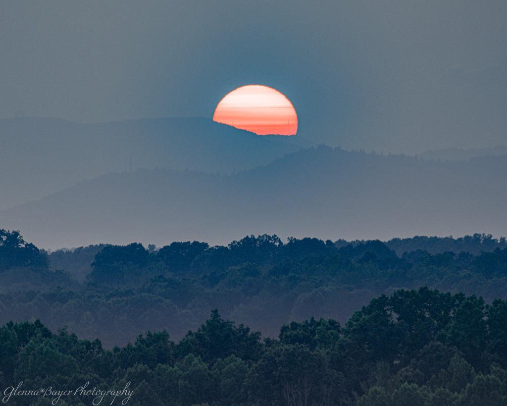sun dipping below blue distant mountains