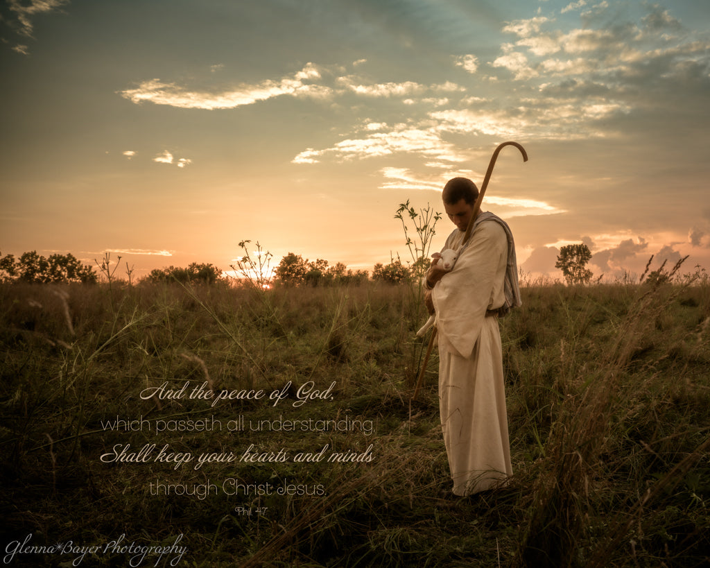 Person in a white robe holding a lamb and staff in a field with a sunset sky