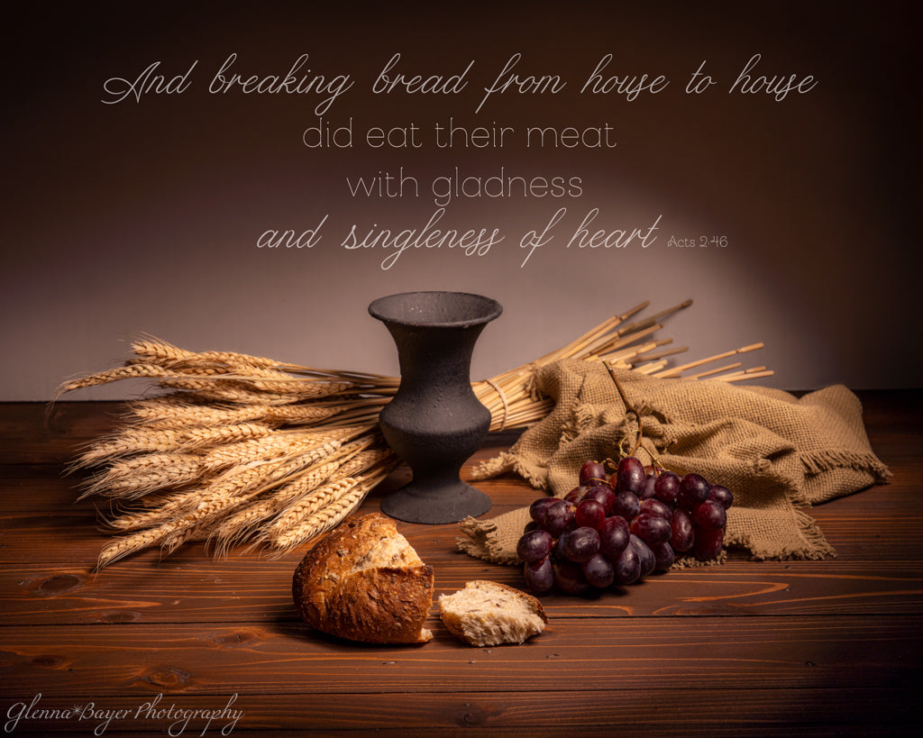 Still life with bread, grapes, vintage wine goblet and wheat on a wooden surface with a Bible verse.