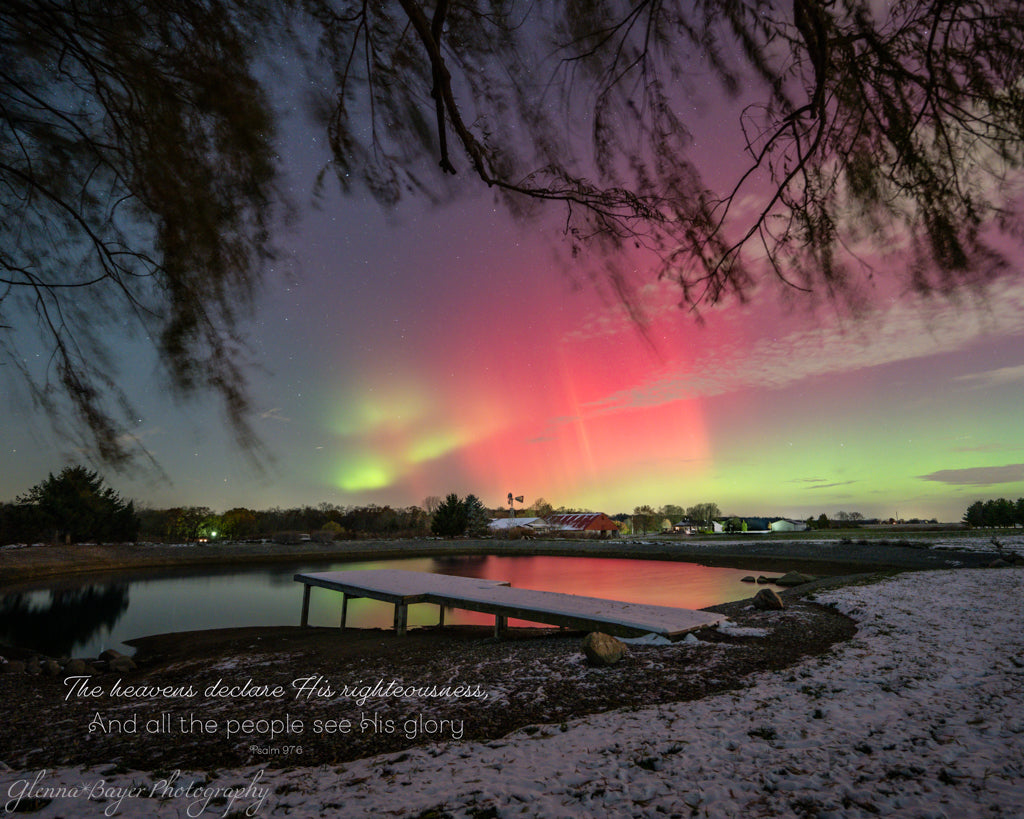 Aurora borealis over a pond with a dock and trees in the foreground.
