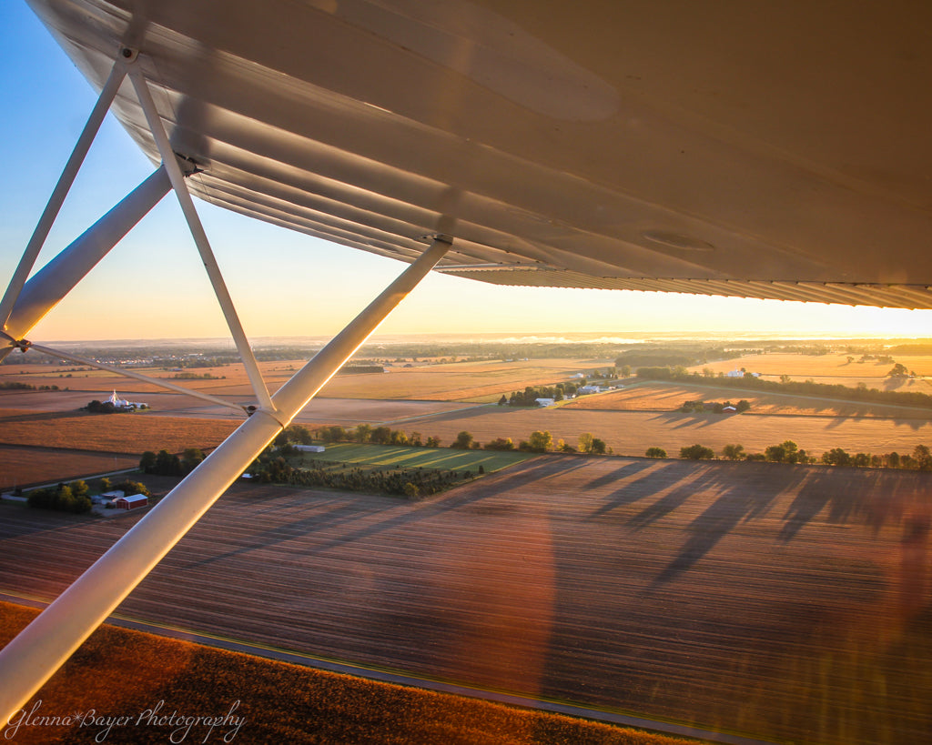 Aerial view from an airplane over a landscape with fields and trees at sunset.