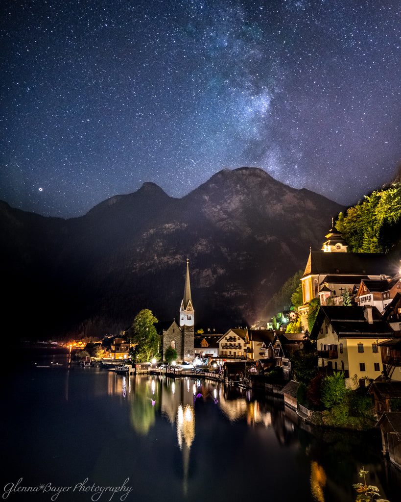 Town by a lake under a starry night sky with mountains in the background