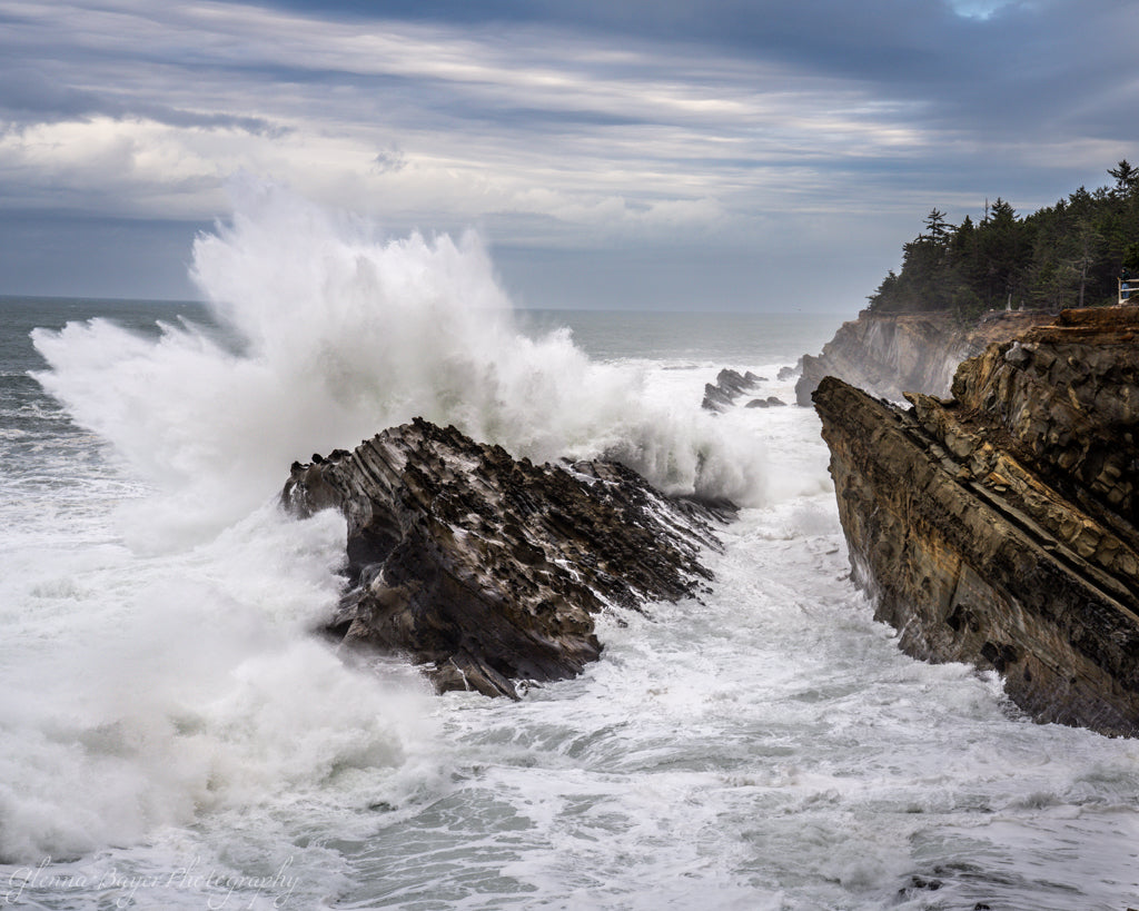 Powerful waves crashing against rocky cliffs with a cloudy sky.