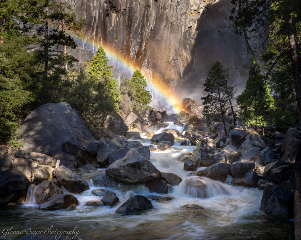 Stream flowing through a rocky landscape with a rainbow in the background