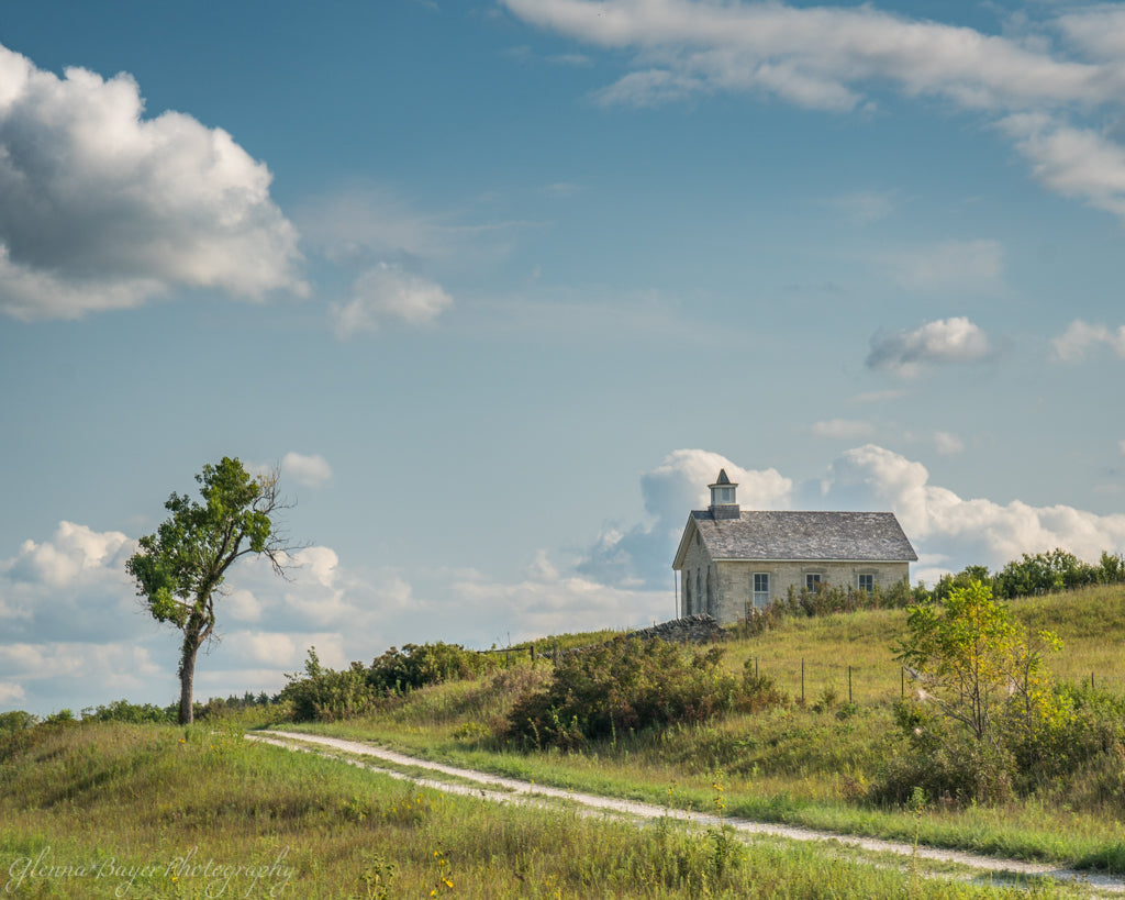 Old single room schoolhouse with gravel road and lone tree in the Flint Hills of Kansas