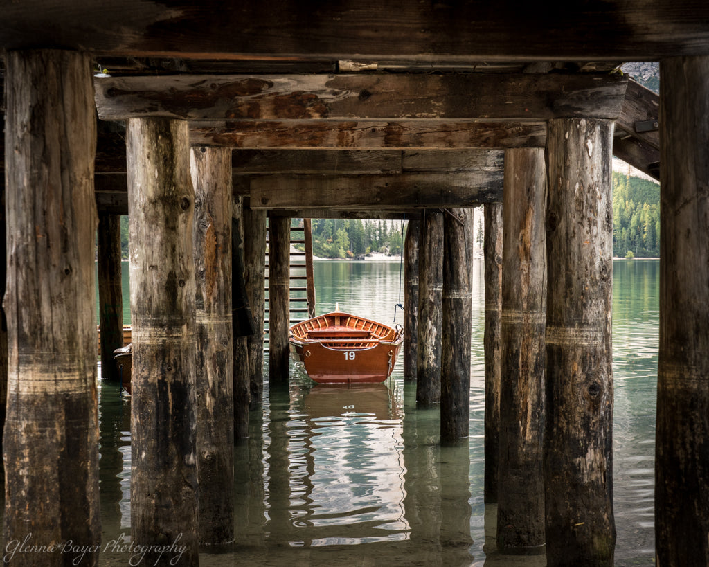 Orange boat under wooden pier on Lake Braies in Dolomites Italy