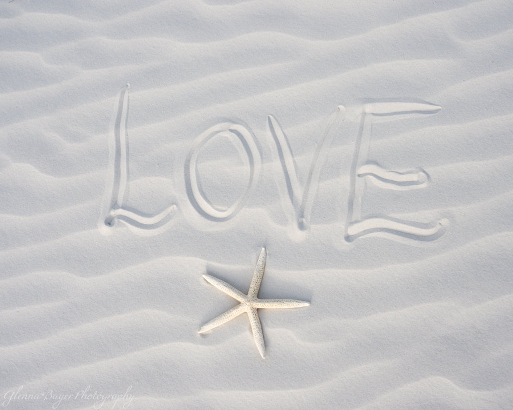 Love written in white sand next to starfish