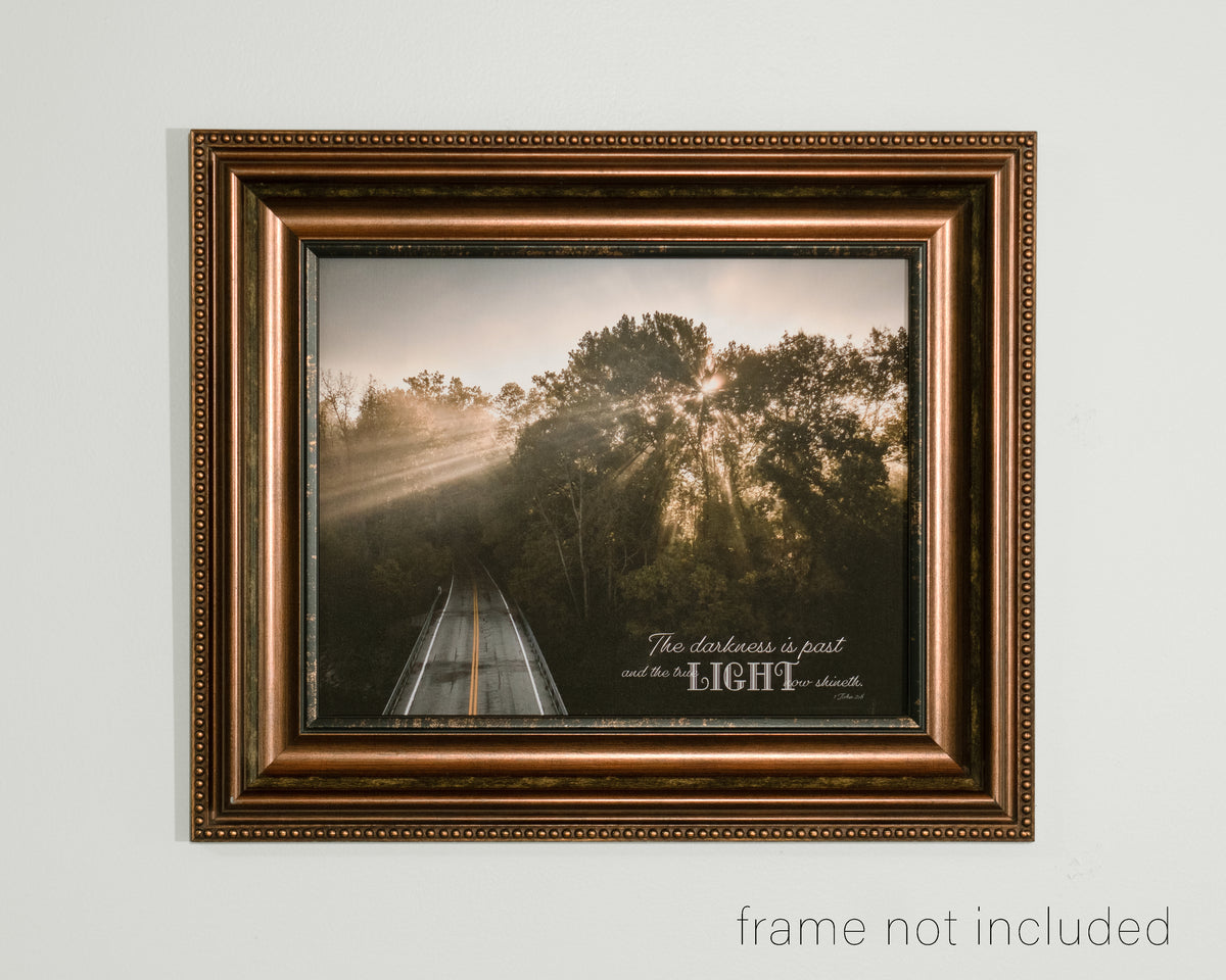 framed print of Arial of road going into woods and light shining through trees