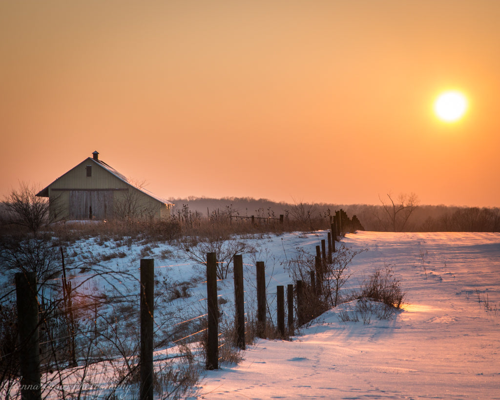Old barn and fence row in snow with orange sunset