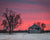 Old wooden barn in snow against dramatic pink sunset