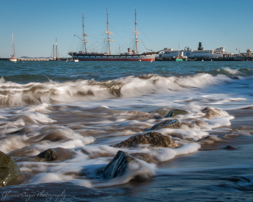 Waves rushing over rocks on beach and boats docked in San Francisco, California morning